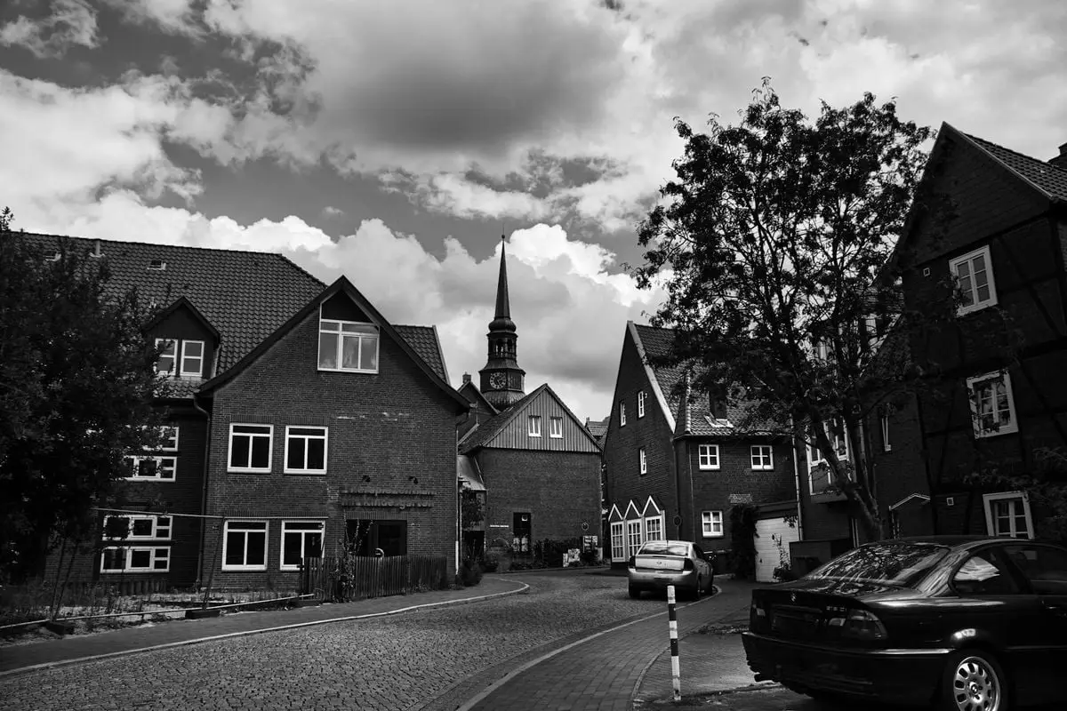 Black and white photo of a quaint town street with traditional houses and parked cars.