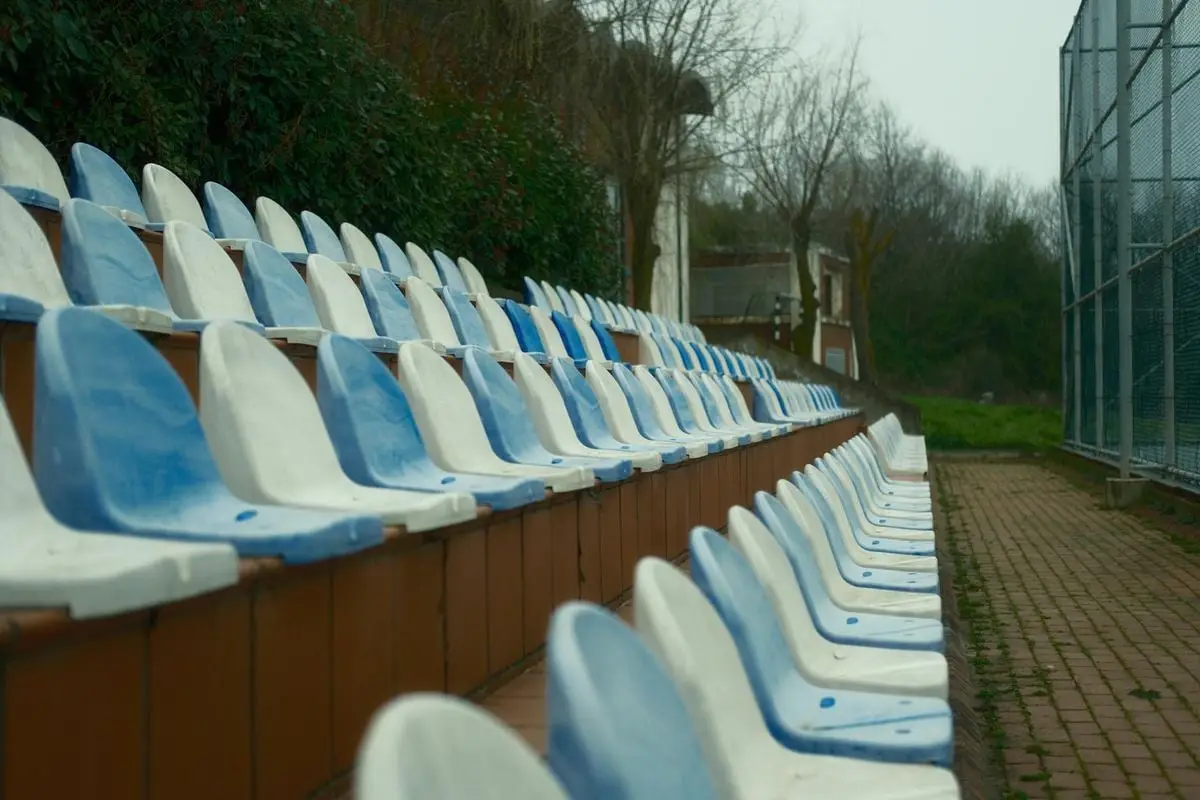 Row of empty blue and white stadium seats outdoors in an overcast setting, suggesting a sports venue.