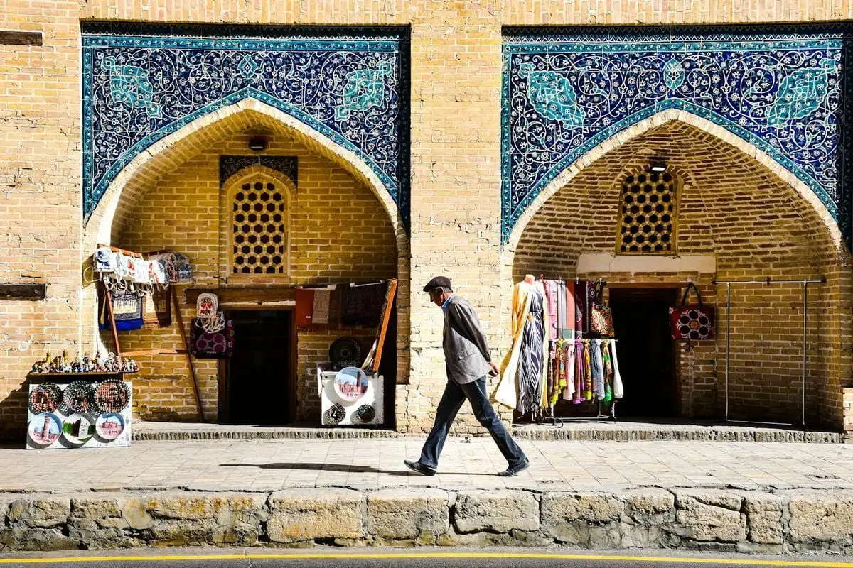 Man walks past vibrant mosaic storefronts in Bukhara, Uzbekistan, showcasing traditional architecture.