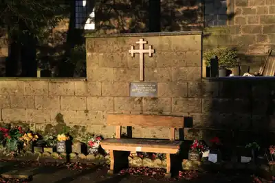 Tranquil cemetery scene with wooden bench, flowers and memorial plaque in sunlight.