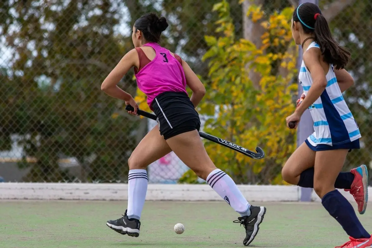 Teen girls engaged in an intense field hockey match on an outdoor court.