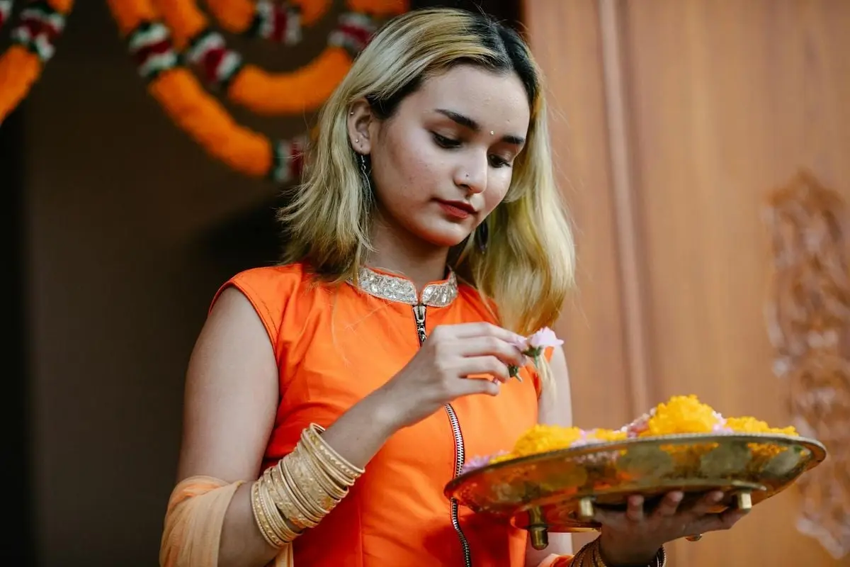 Young Indian woman in traditional attire holding a decorative platter with flowers, celebrating a festival.