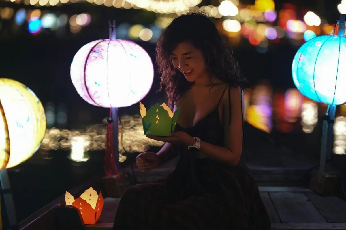 A young woman enjoys an illuminated boat ride surrounded by colorful lanterns at night.