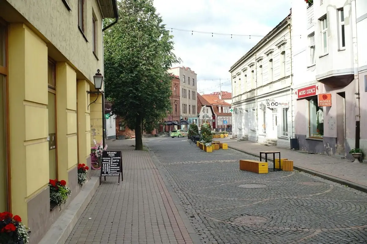 Picturesque cobblestone street scene of a quiet European town with historical architecture and tree-lined sidewalks.