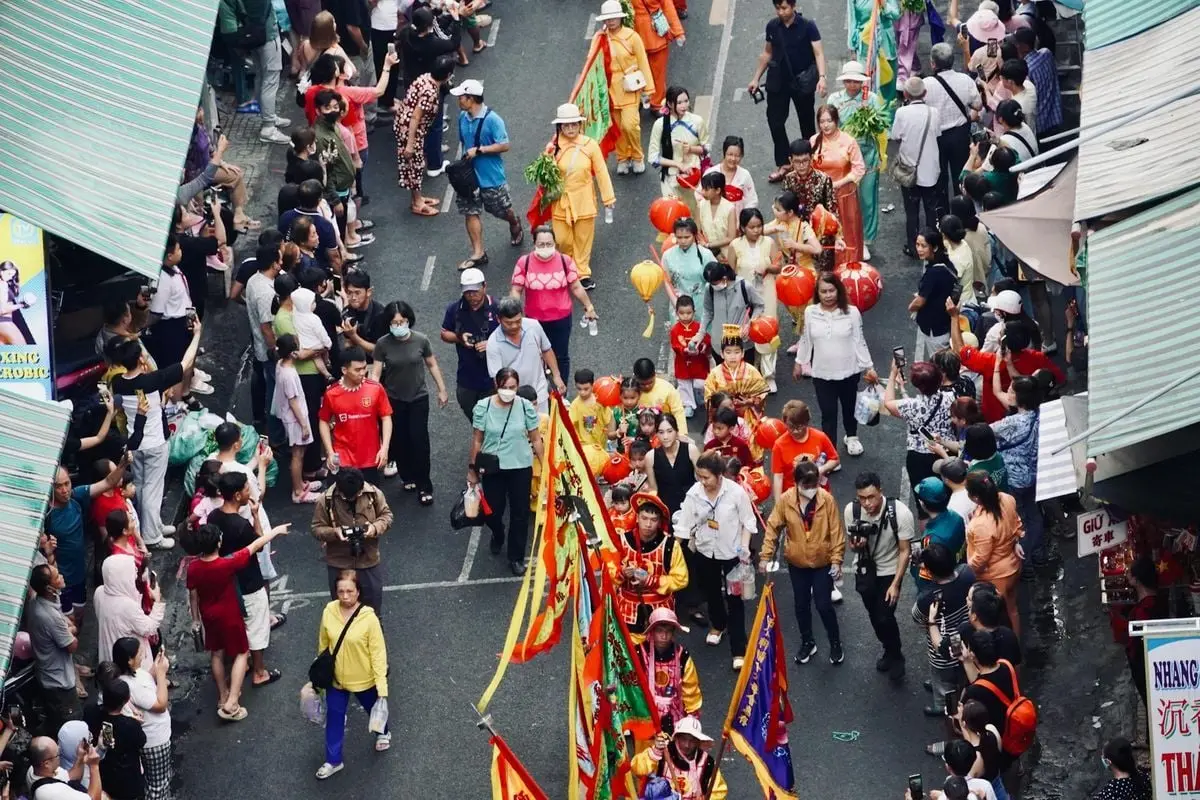 Colorful street festival parade with participants and onlookers celebrating with flags and lanterns.
