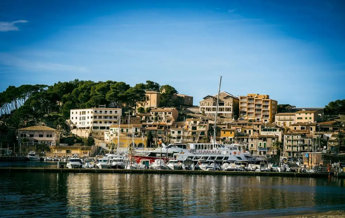A picturesque Mediterranean town with a bustling marina and lush hills in the background.