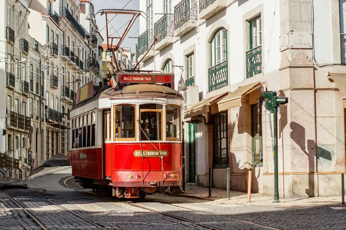 A classic red tram traverses the charming and narrow streets of Lisbon, Portugal, under the bright day sun.