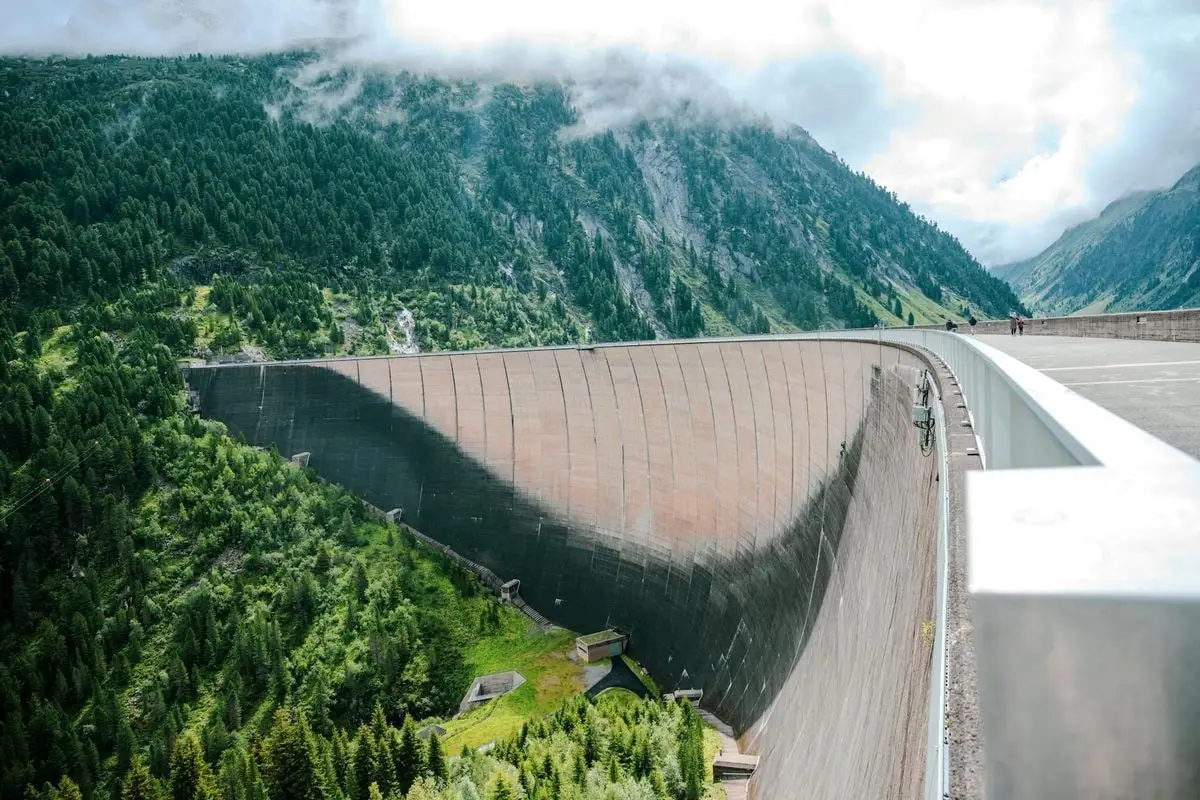 Breathtaking view of a massive dam surrounded by lush green forests in the Tyrolean Alps, Austria.