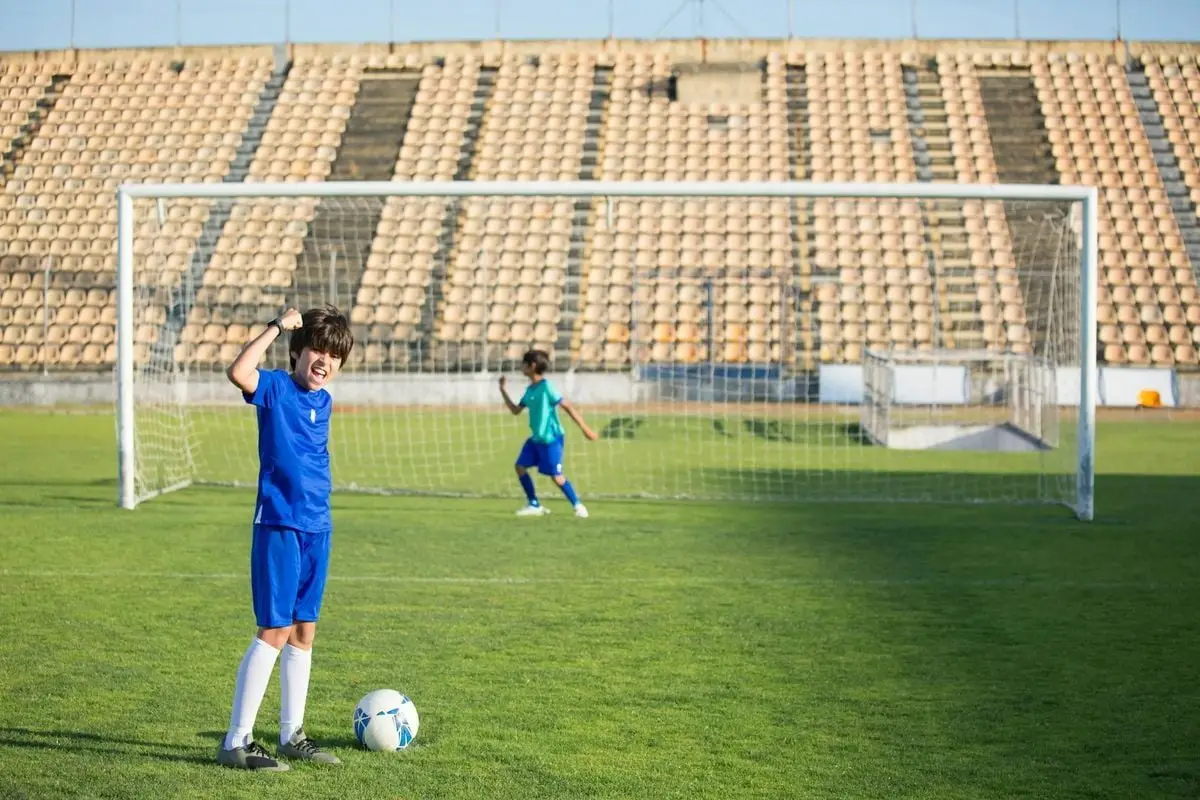 Joyful kids playing soccer in an empty stadium on a bright day, celebrating a successful goal.