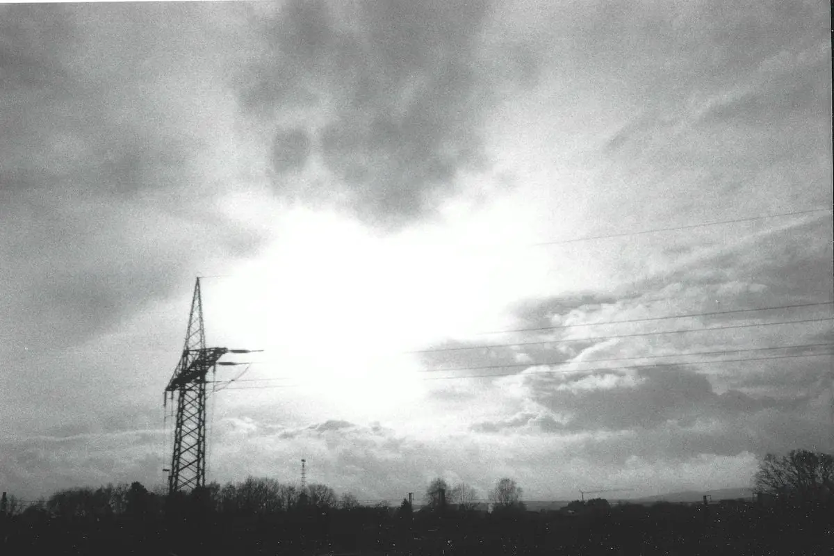 Silhouetted power line tower against the dramatic sky in black and white, depicting energy infrastructure.