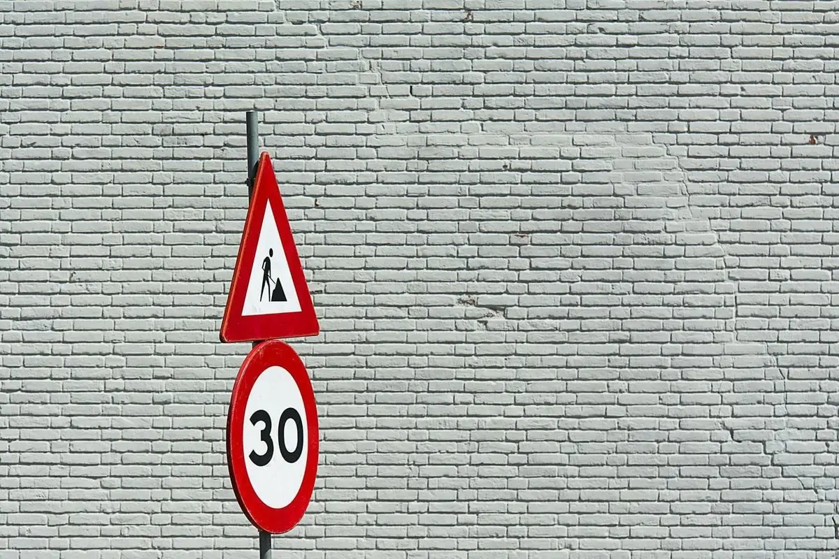 Traffic signs with speed limit and construction warning against a brick wall background.