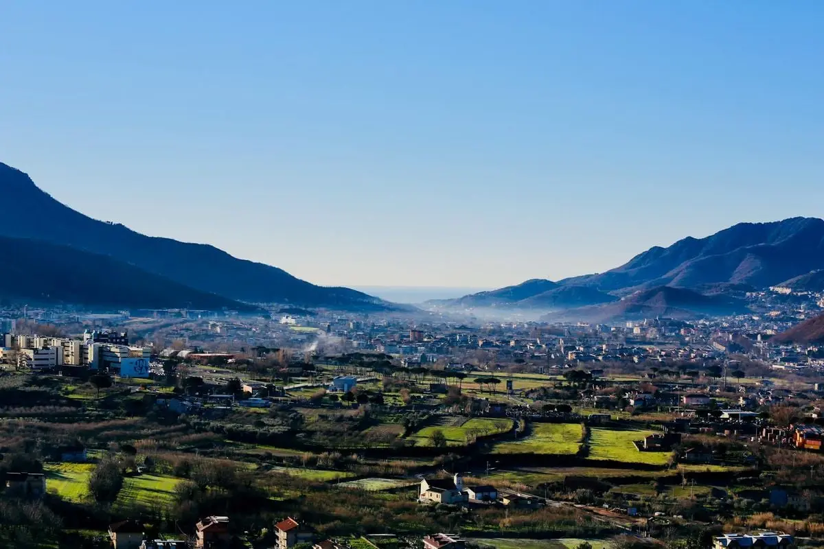 Explore the serene landscape of Fisciano, Italy, featuring mountains, valleys, and a picturesque town under a clear blue sky.