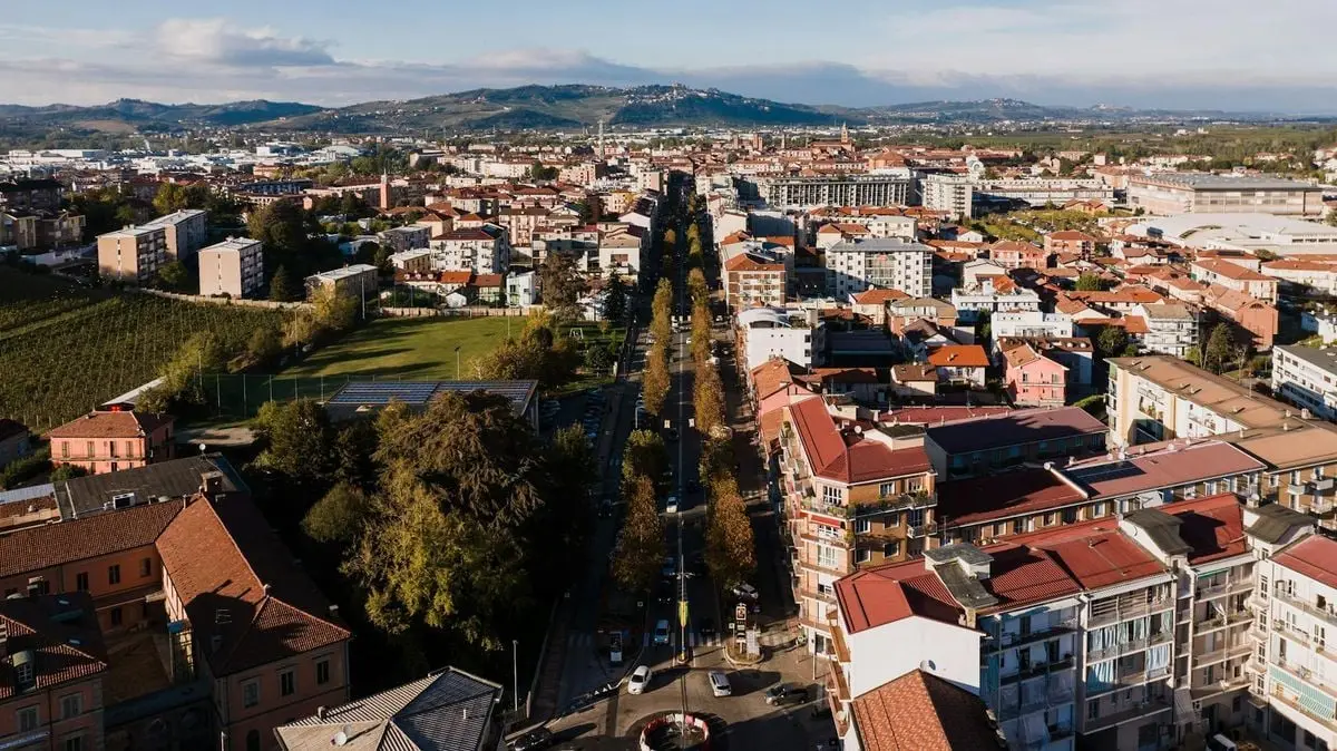 Aerial perspective of Alba's residential area in Italy, lined with trees and hills.