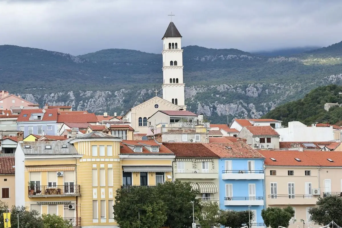 Picturesque coastal town with vibrant buildings and a historical church tower against a mountain backdrop.