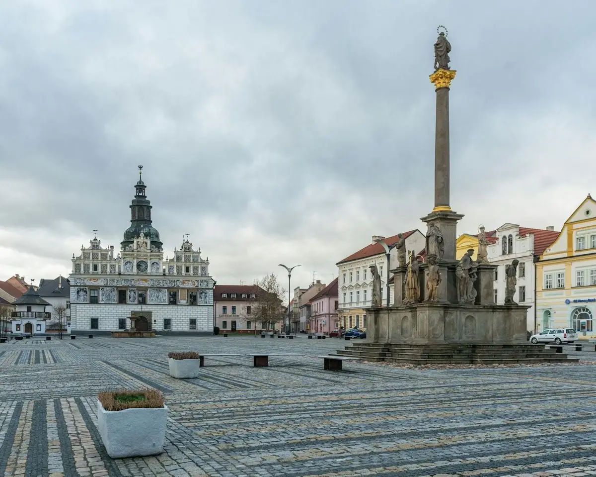 A scenic view of a historic town square with a prominent monument and ornate buildings.