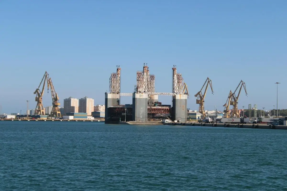 A panoramic view of Cádiz harbor featuring industrial cranes and a city skyline.