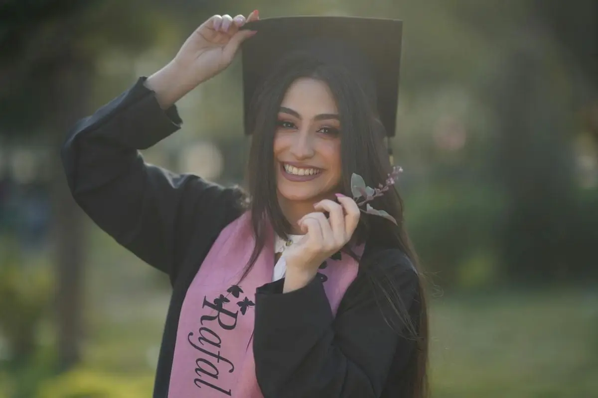 Young graduate woman smiling in cap and gown, celebrating her success outdoors.