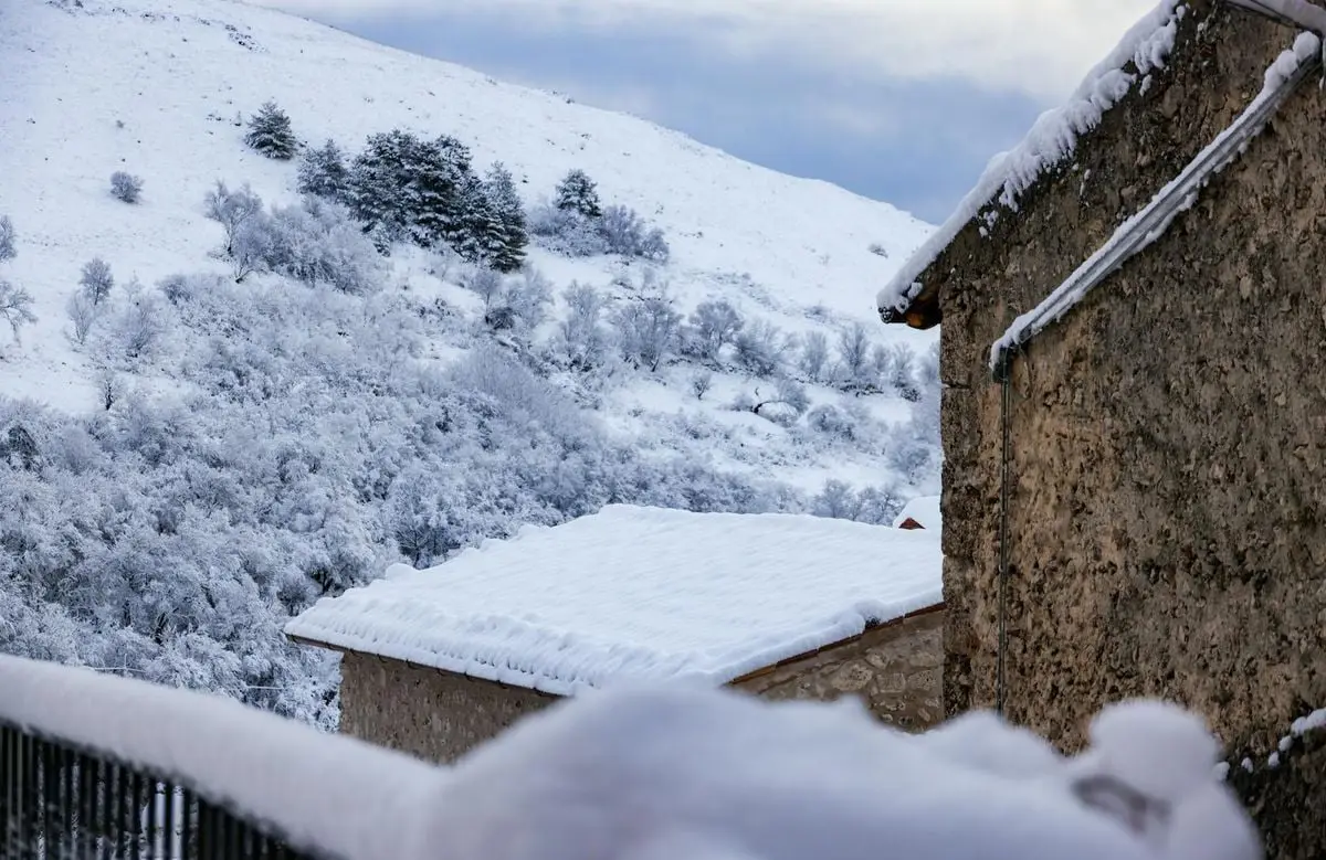 Picturesque winter view of a snow-covered village with rustic stone houses and serene landscape.