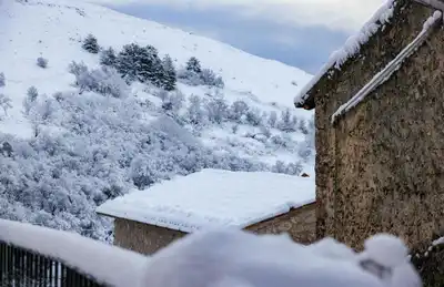 Picturesque winter view of a snow-covered village with rustic stone houses and serene landscape.