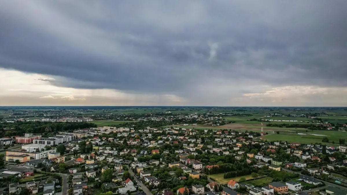 Aerial view of a small countryside town with expansive clouds above and surrounding landscapes.