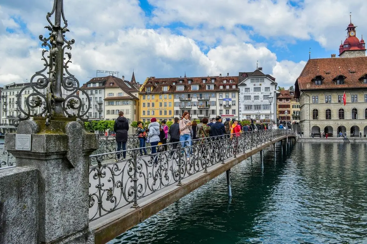 People walking on aged pedestrian bridge with decorative elements crossing river channel and leading to old town in daytime