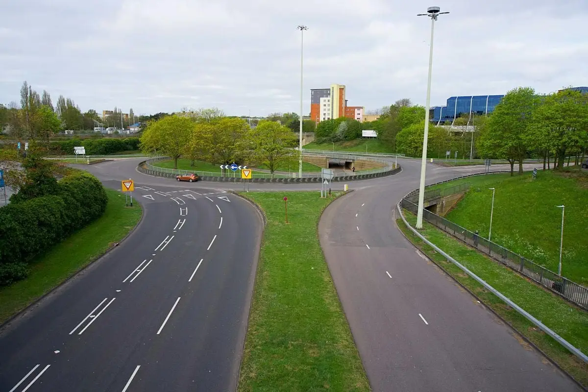 Roundabout with clear road markings surrounded by greenery and buildings in the background.
