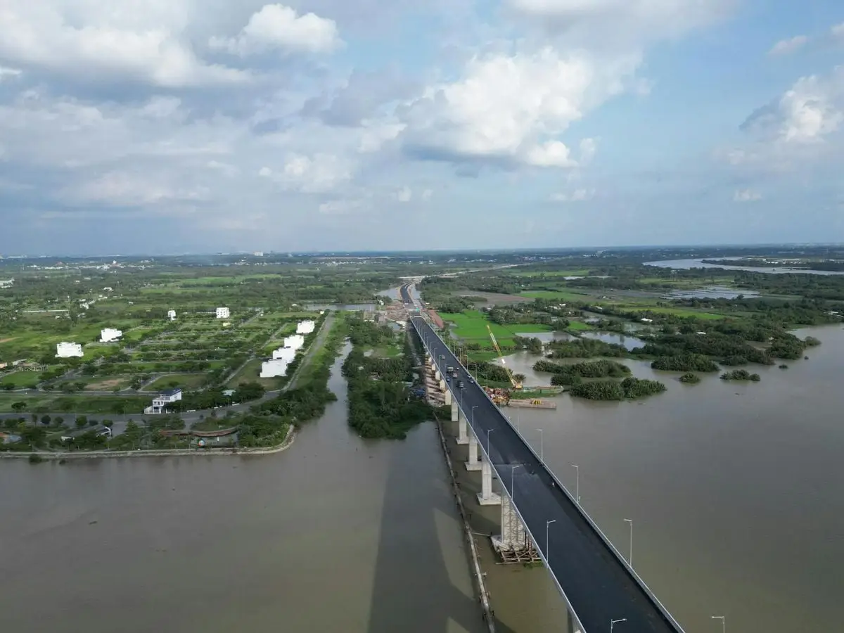 Aerial shot of bridge over river in Dong Nai, Vietnam with green landscapes and cloudy sky.
