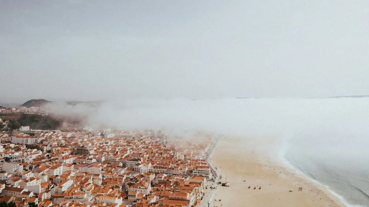 Aerial view of Nazaré's beach and red-roofed buildings enveloped in fog.