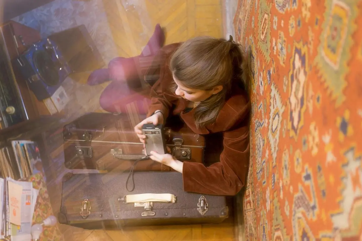 Woman with a retro camera resting on vintage suitcases, evoking nostalgia in a cozy indoor setting.