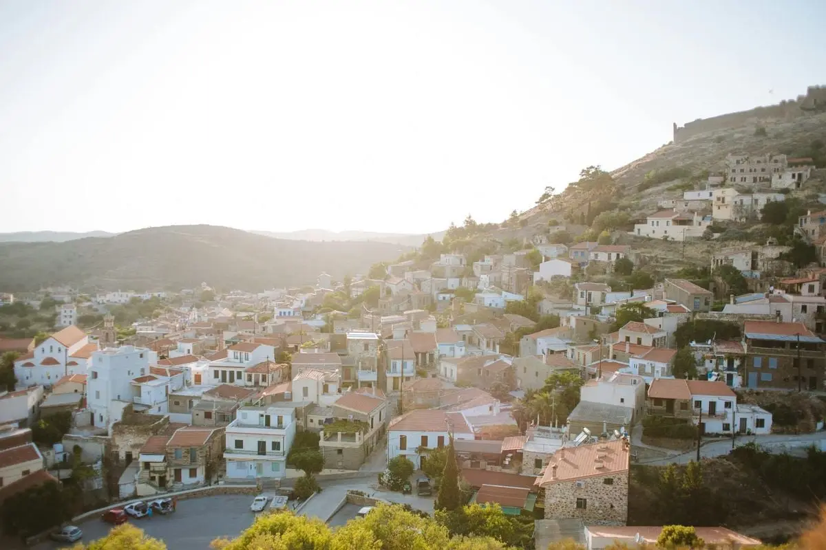 A serene aerial view of a Greek old town with houses on a hillside during sunset, offering a picturesque landscape.