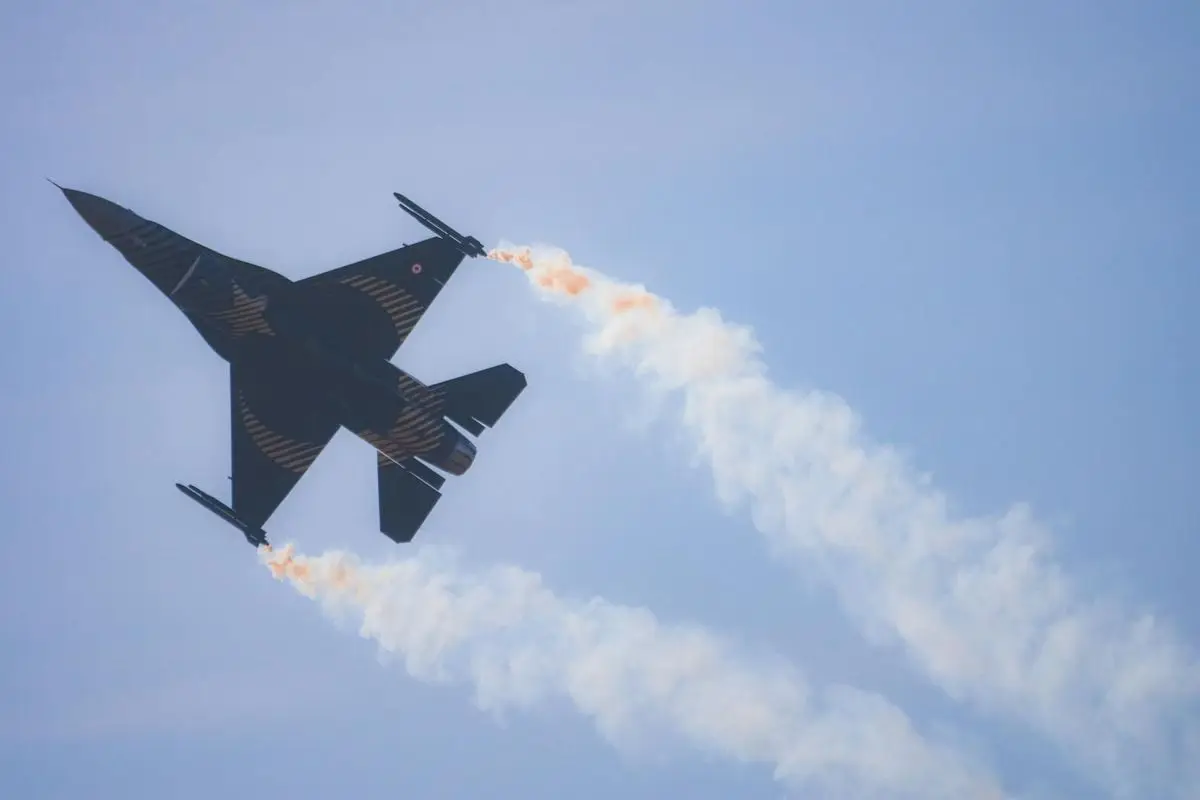 Jet fighter performing aerobatics with visible smoke trails against blue sky.