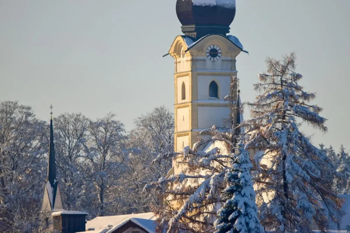 Picturesque Bavarian church in snowy winter, surrounded by snow-covered trees in Schnaitsee, Germany.