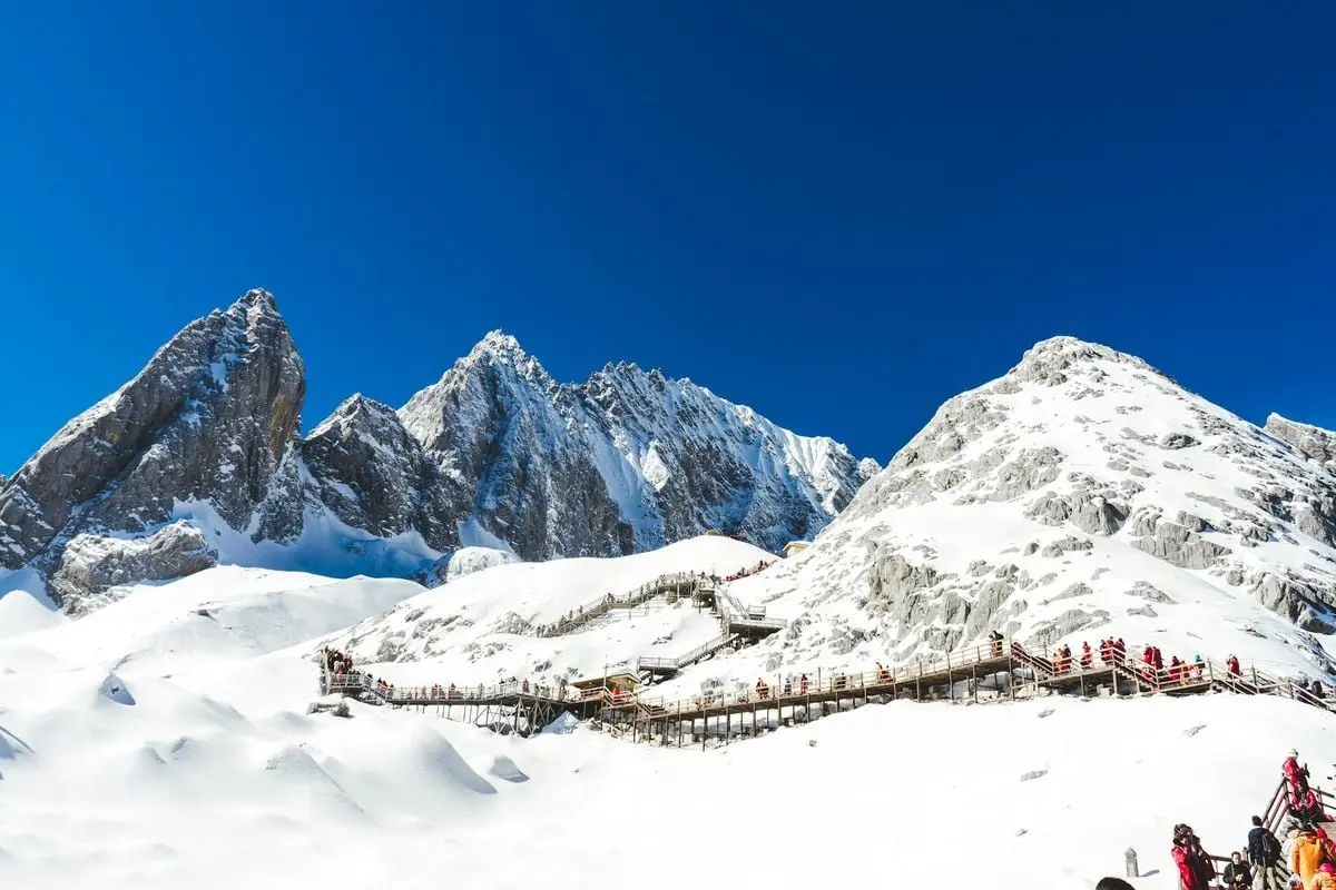 Snow-covered mountain with wooden walkway under clear blue sky in Lijiang, China.