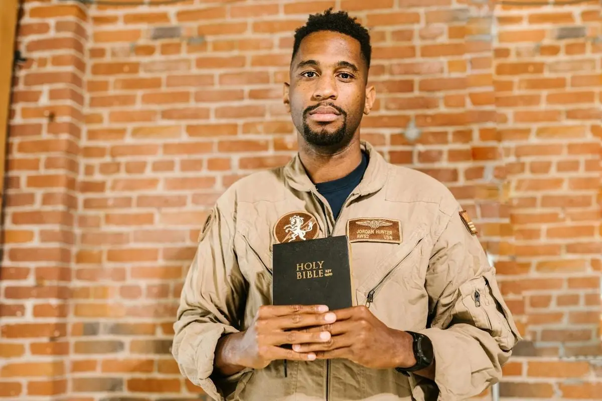 A military veteran holding the Holy Bible in front of a brick wall background.