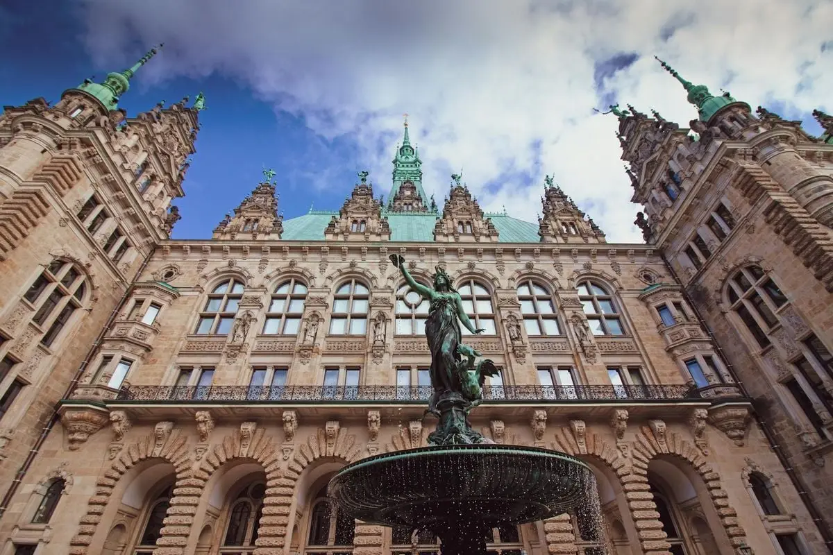 Stunning view of Hamburg Town Hall and fountain under a vibrant sky.