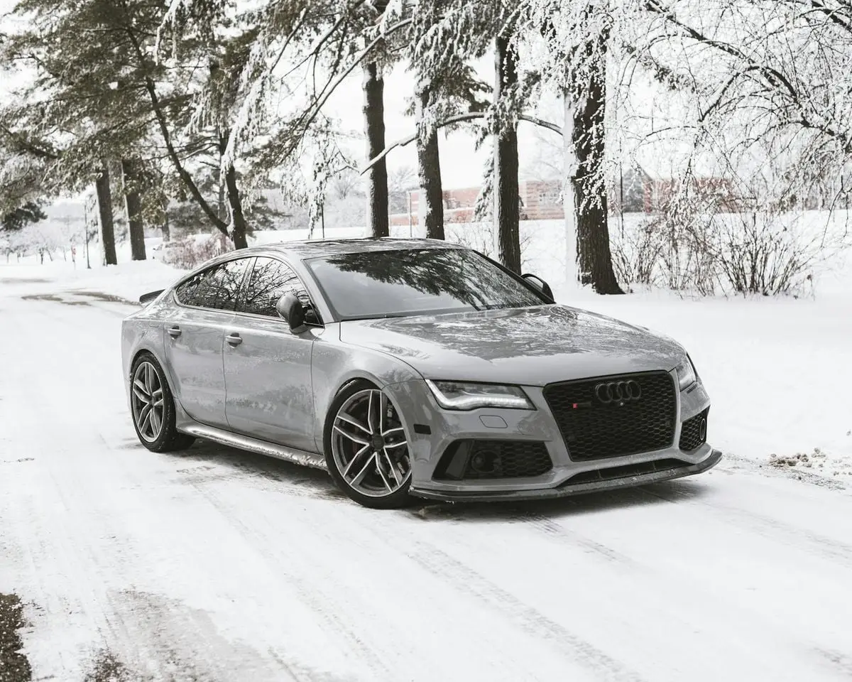 A sleek luxury car parked on a snowy road surrounded by trees in a winter landscape.