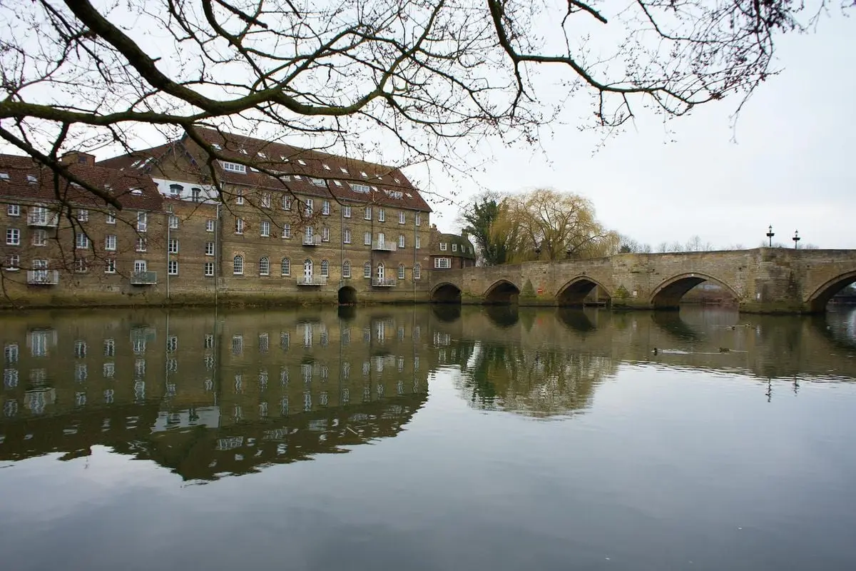 Serene view of historic bridge and buildings reflecting in the River Great Ouse in Godmanchester, England.