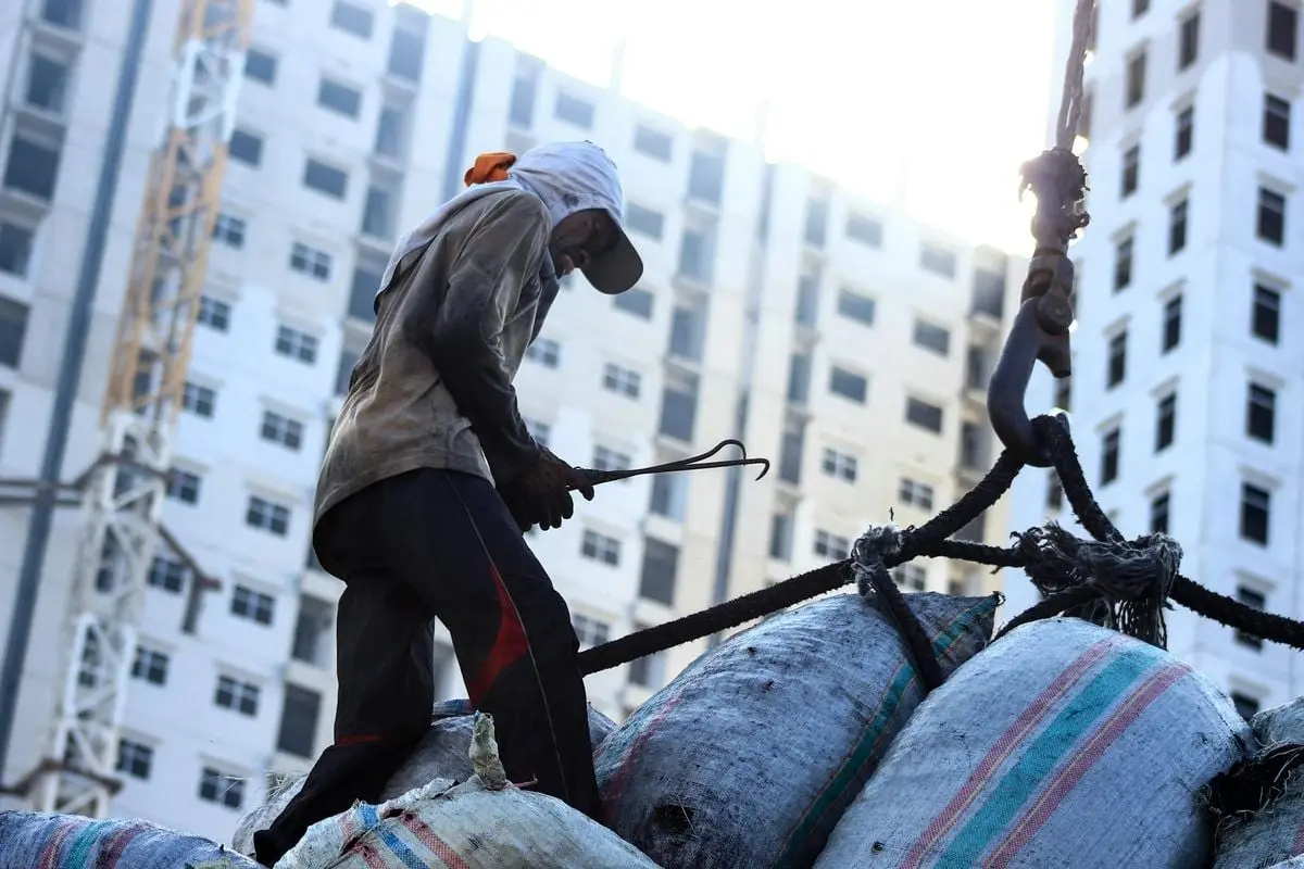A construction worker manages crane load with sacks at an urban site in Jakarta.