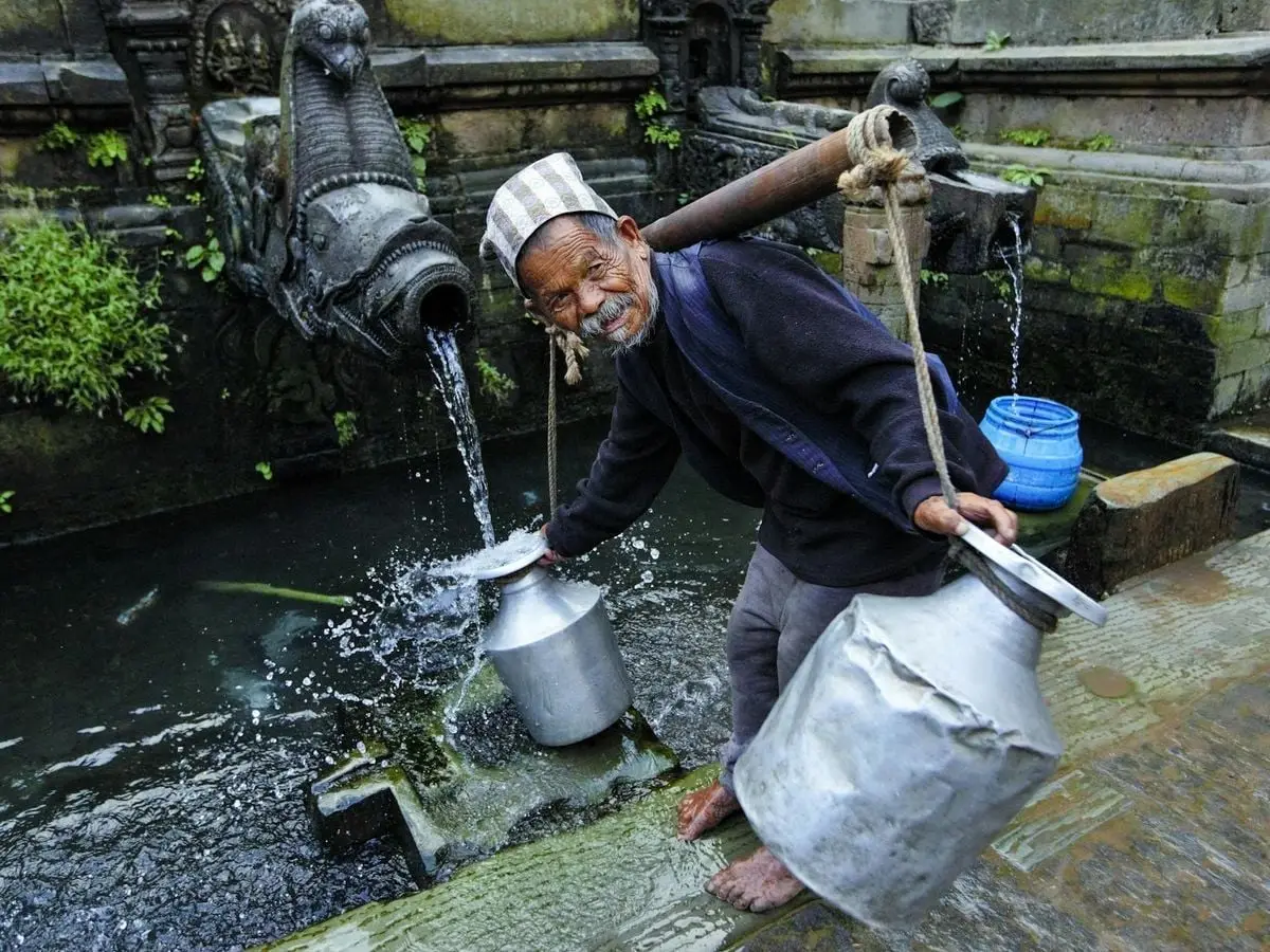 Elderly man collecting water from traditional fountain, showcasing cultural heritage.