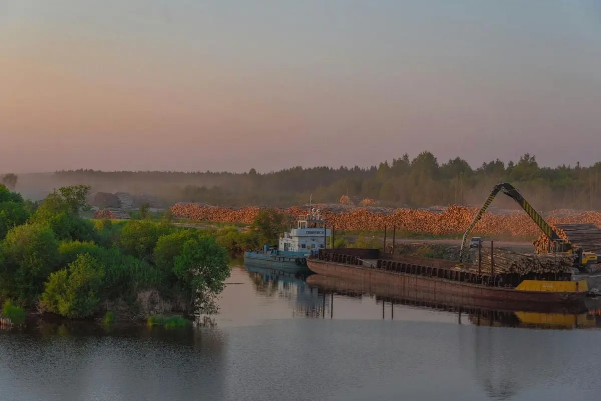 Peaceful riverside landscape in Russia with a cargo ship and industrial crane at dusk.