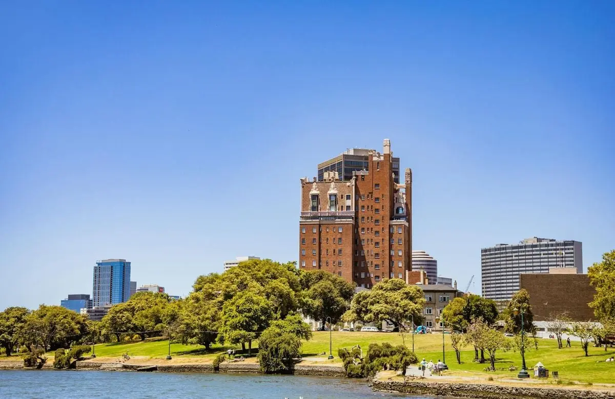 A tall historic brick building overlooking a park and waterfront under a clear blue sky.