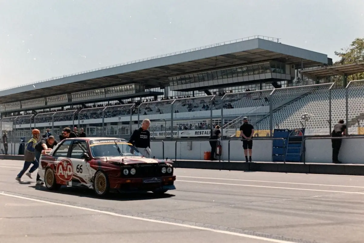 Vintage race car being pushed by crew at outdoor raceway on a sunny day.