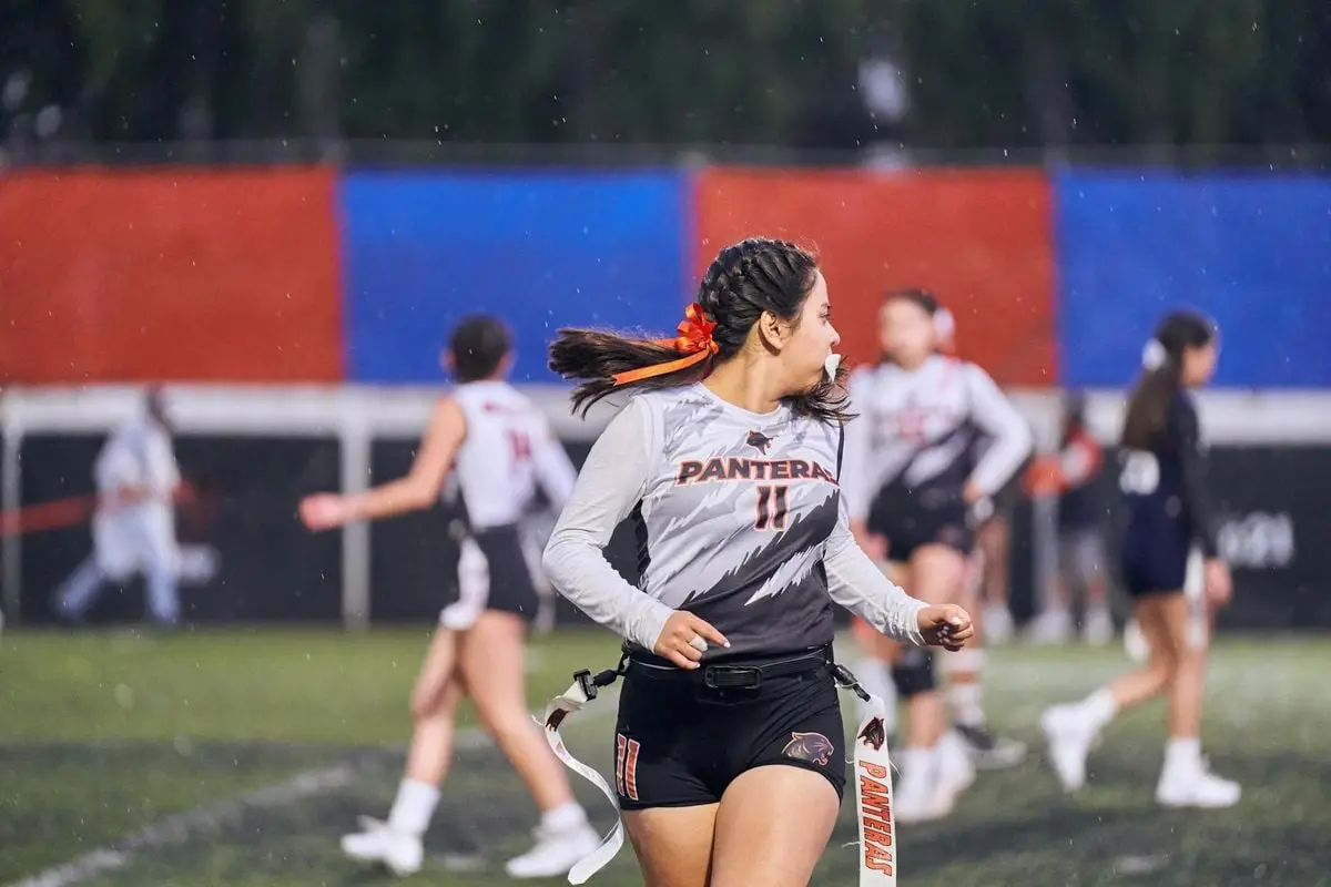 A young woman in sports attire plays flag football under the rain, showcasing athleticism and teamwork.