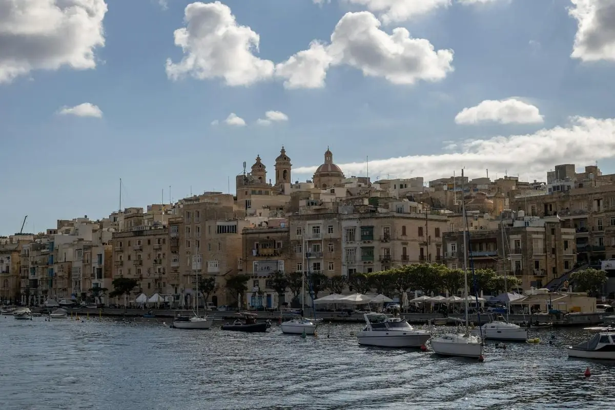 Idyllic coastal view of a Mediterranean town with boats docked at the waterfront under a cloudy blue sky.