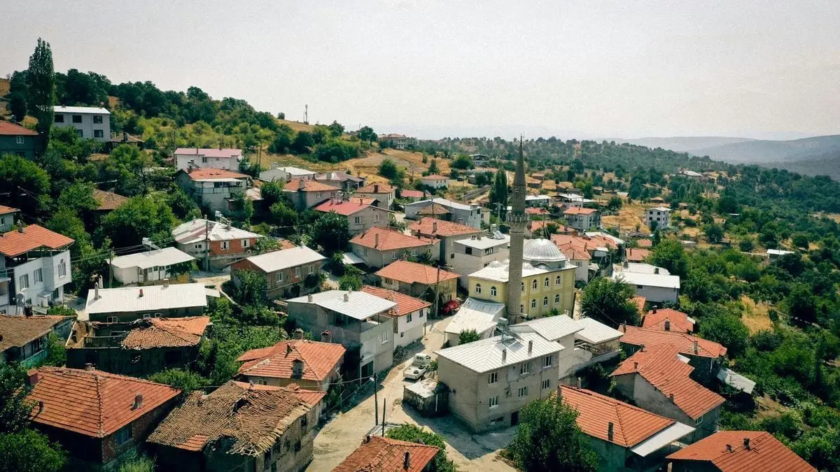 A scenic aerial view of a village in Bursa, Türkiye, showcasing red-roofed houses surrounded by lush greenery.