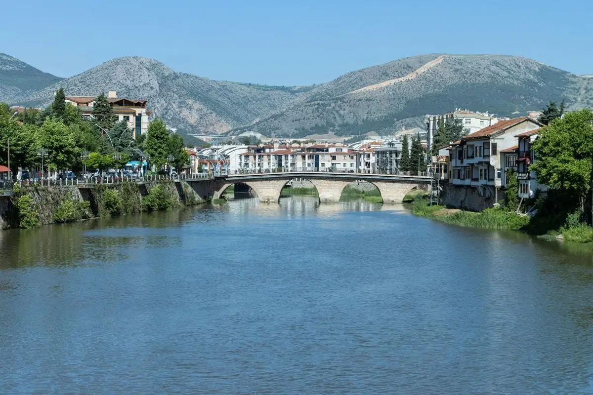 Scenic view of an ancient stone bridge over a serene river in Amasya, Turkey with lush greenery.