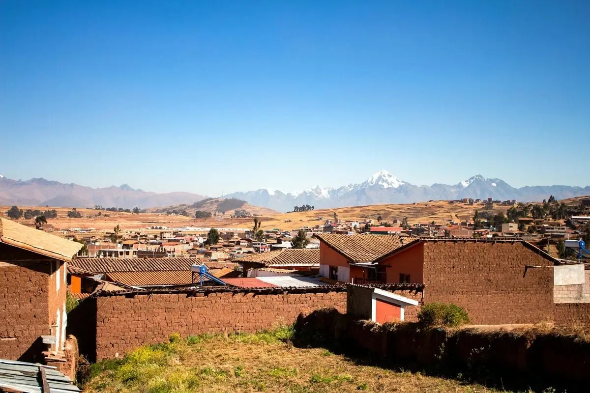 Rustic townscape of Cusco, Peru with Andean mountains in the background under clear blue sky.
