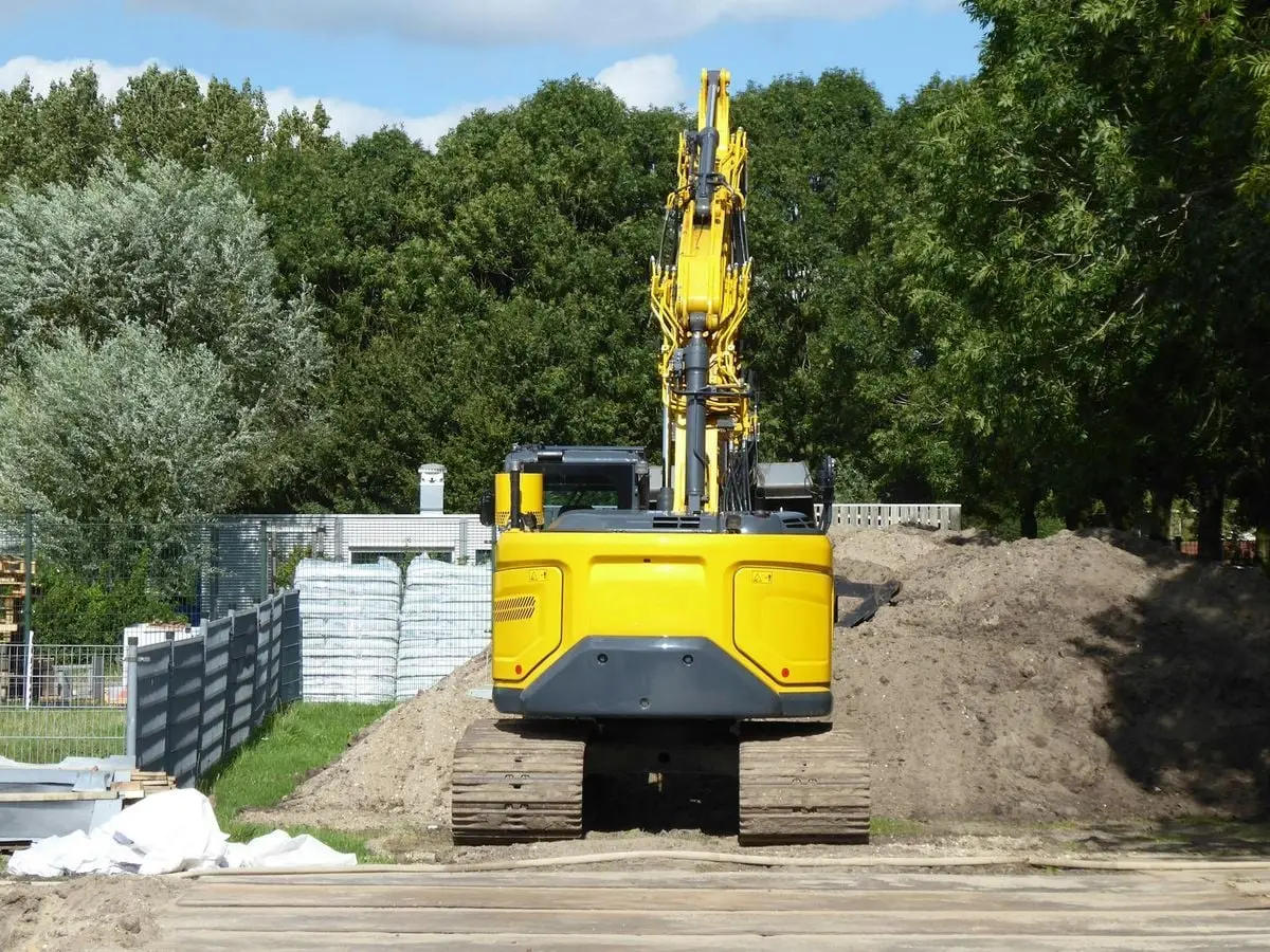 Yellow excavator at a construction site surrounded by green forest on a sunny day.