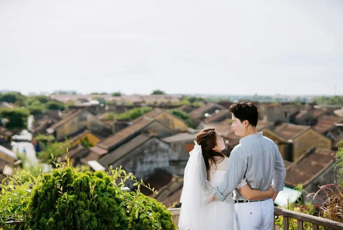 A romantic couple embraces on a balcony overlooking a picturesque European town.