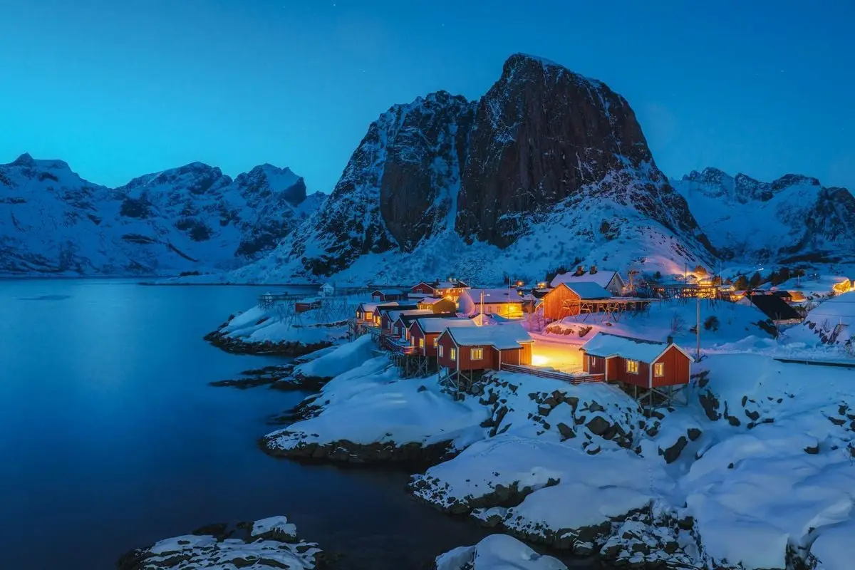 Beautiful aerial view of a snow-covered Norwegian village by the coast at night, surrounded by mountains.